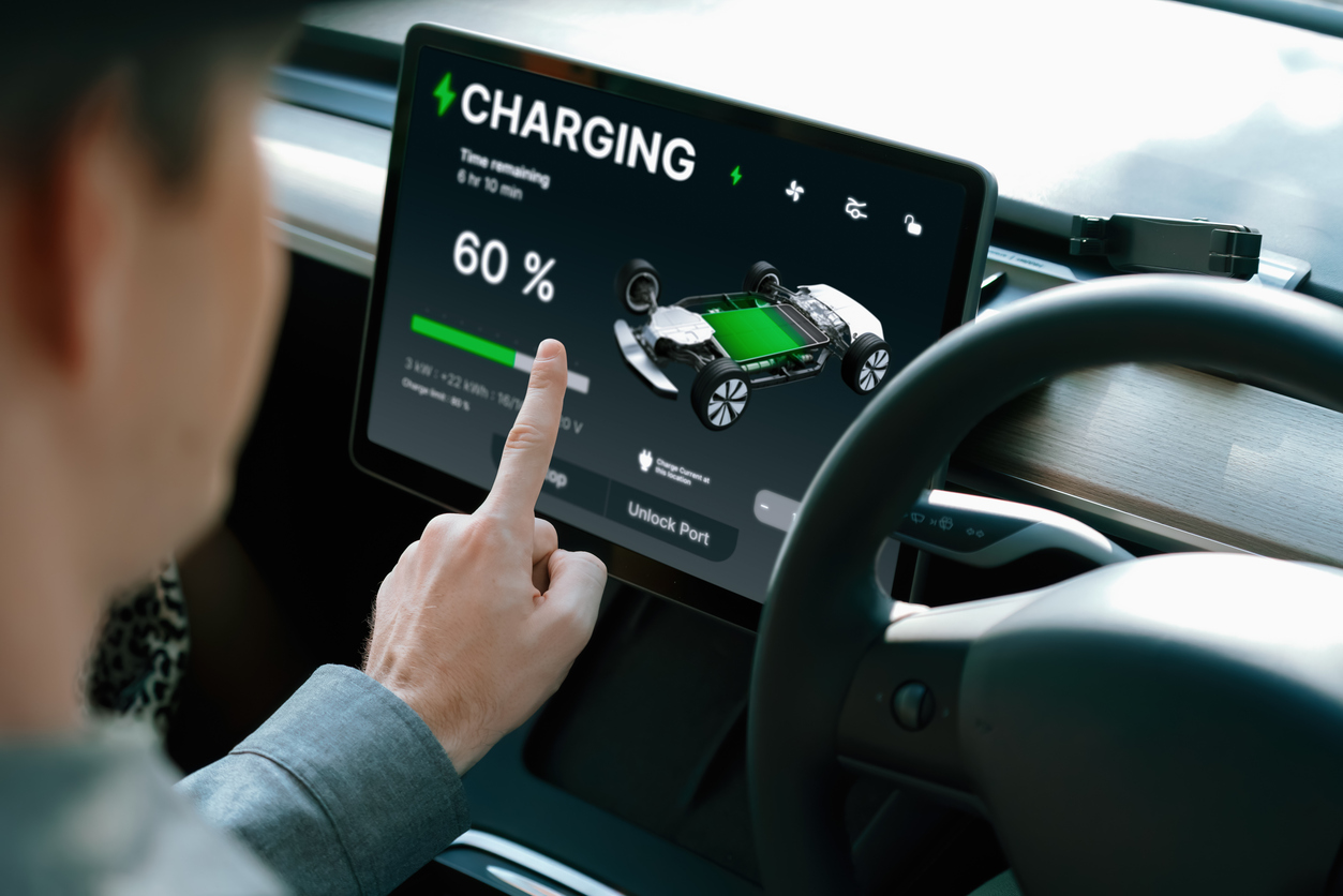 Electric car driver checks battery charging status app screen in car interior