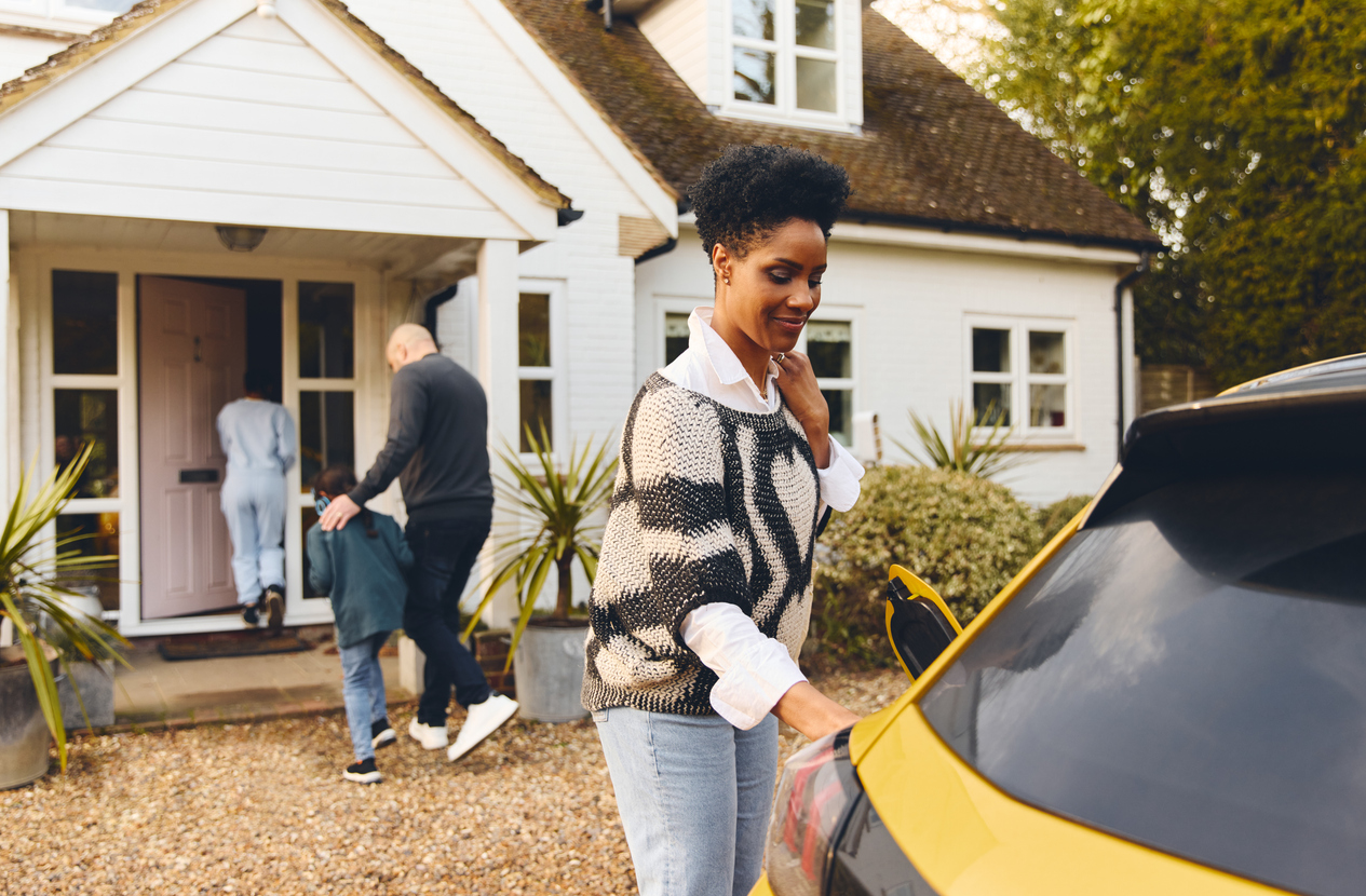 Woman charging electric car in driveway outside house