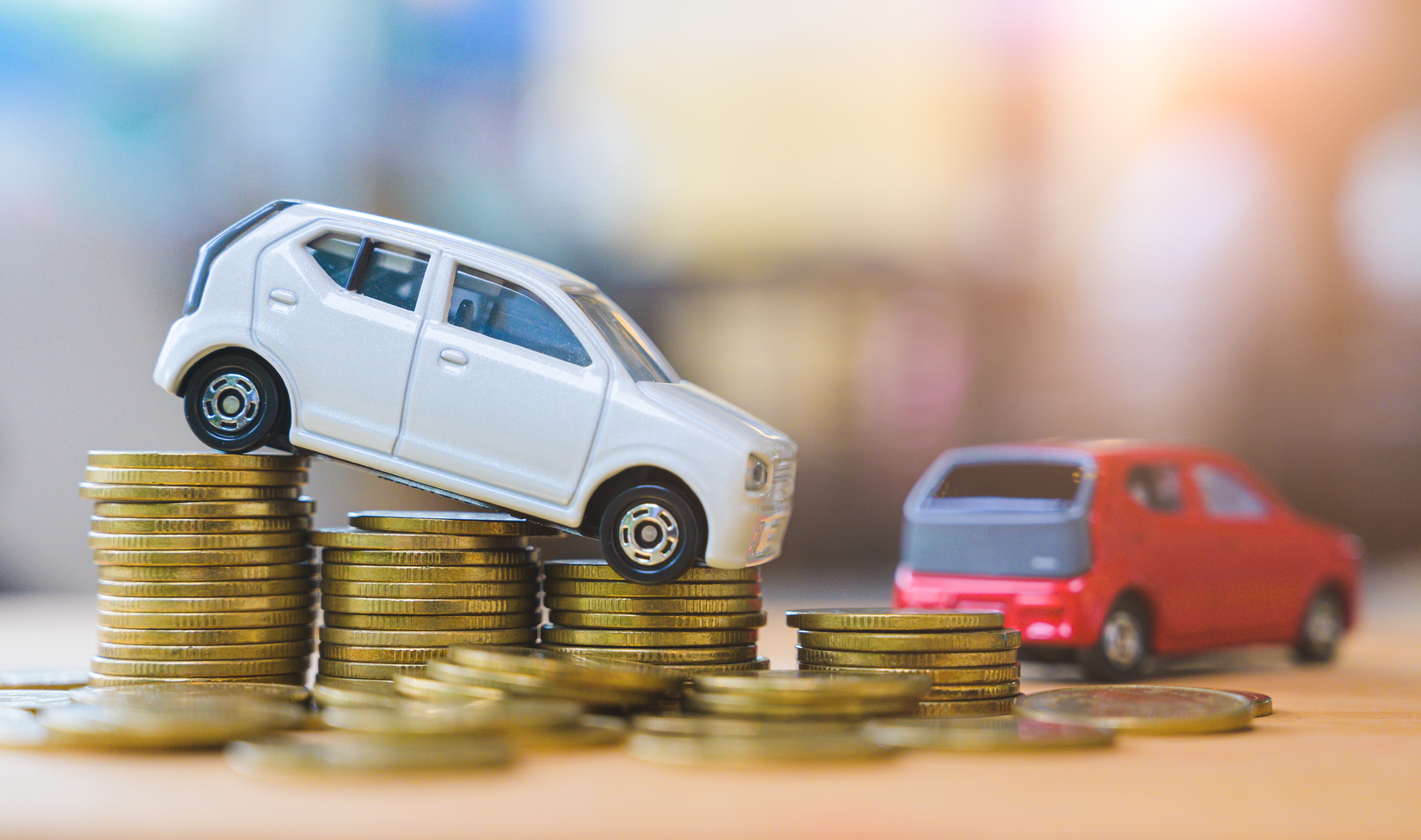 Toy cars on stacked coins representing car value depreciation and financial protection with GAP insurance.